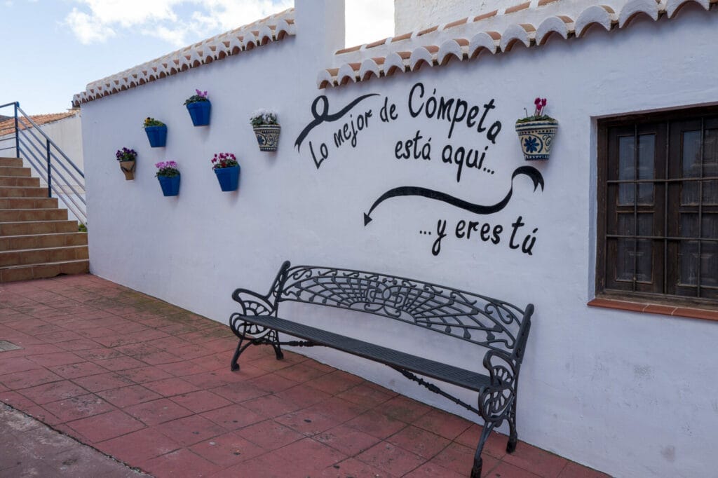Mur blanc, banc, pots fleuris, escalier, inscription espagnole.