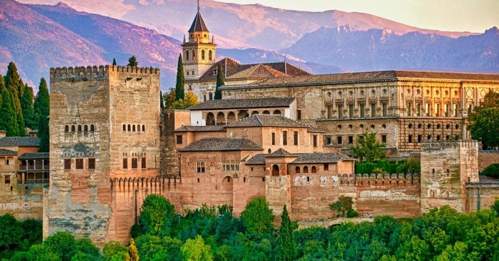 Alhambra Palace at sunset with mountains in background.