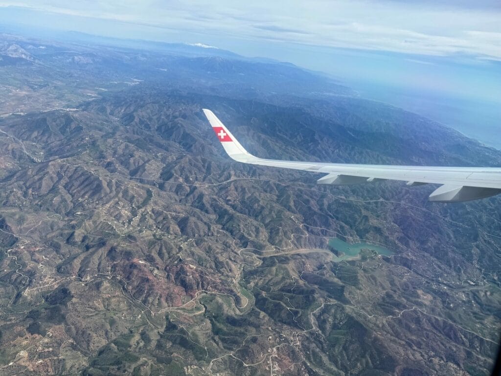 Aircraft wing over mountains with lake and coastline view.