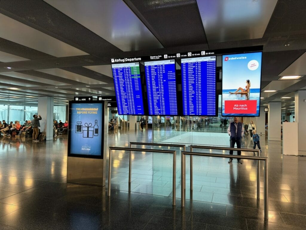 Airport departure board with waiting passengers.
