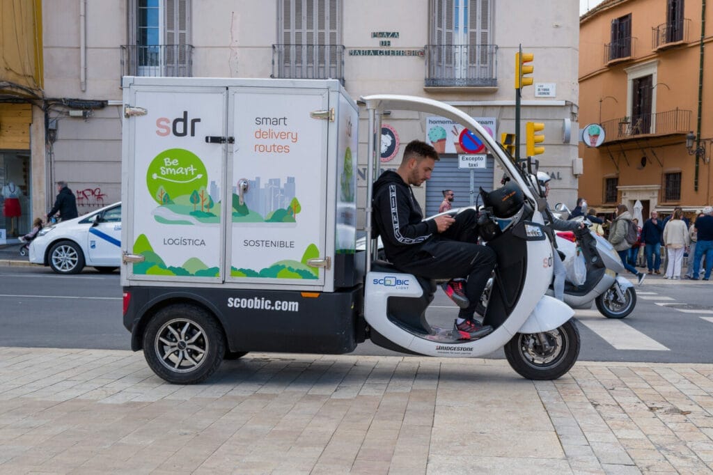 Electric delivery scooter with driver on city street.