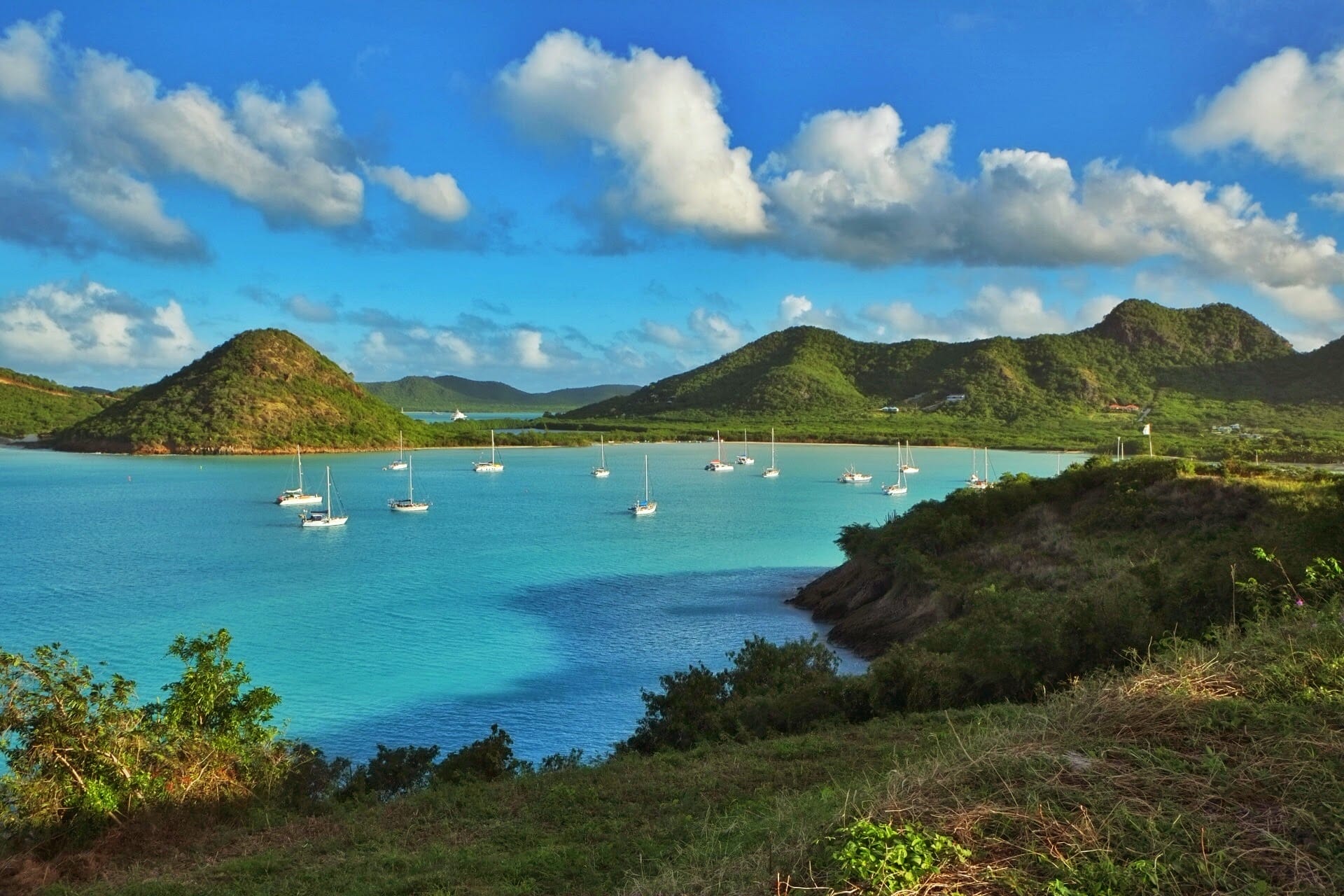 Serene bay with anchored yachts and lush hills.