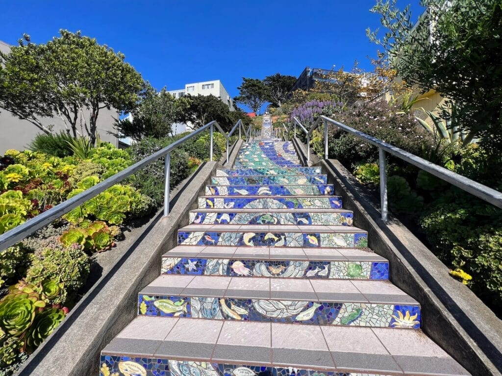 Colorful tiled outdoor stairway with greenery and sky.