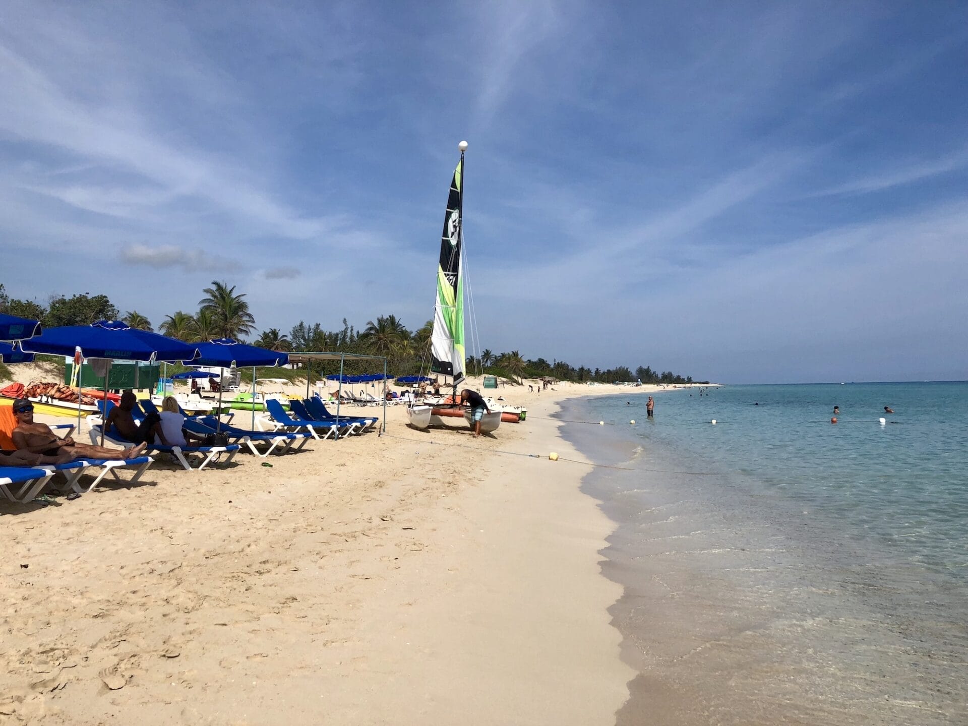 Tropical beach with sailboat and sunbathers.