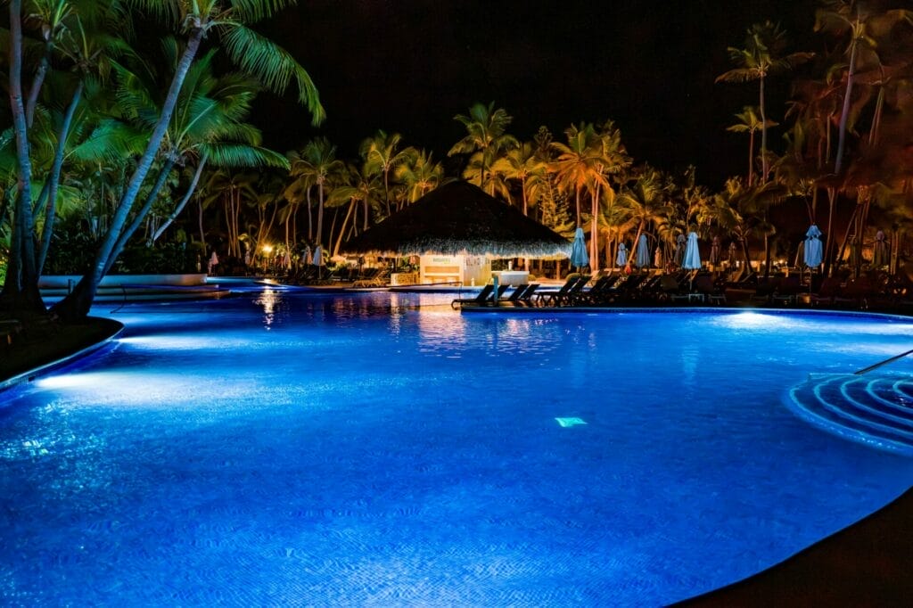 Illuminated resort pool at night with palm trees